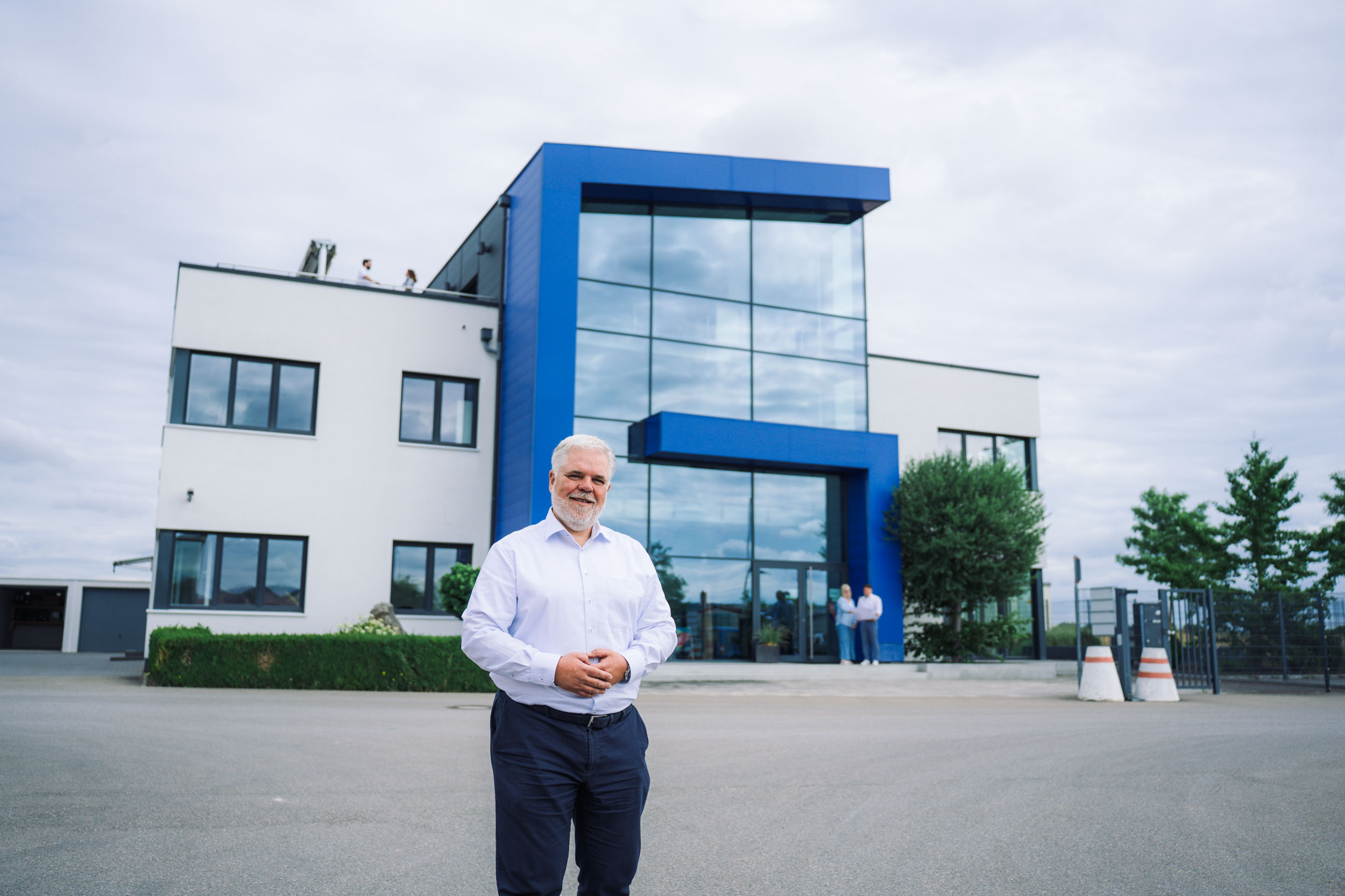 Geschäftsführer von Gerhäuser Bau vor modernem Gewerbebau in Mittelfranken. Innovative Architektur mit blauer Fassade und großflächiger Verglasung.