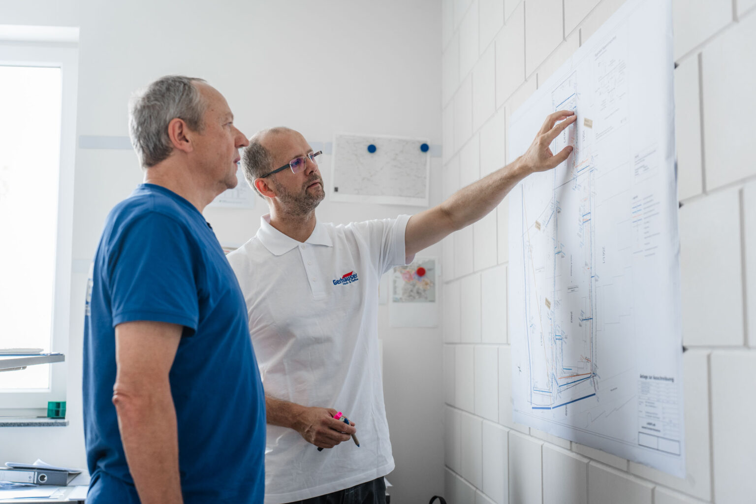 Zwei Mitarbeiter der Gerhäuser Bau Baufirma besprechen Baupläne für einen Hausbau in Mittelfranken an einer Wand.