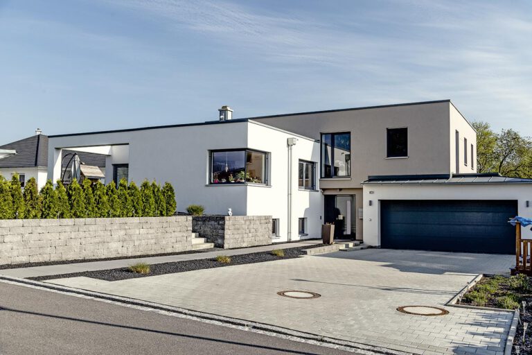 Modernes Einfamilienhaus von Gerhäuser Bau - Massivbau Spezialist aus Franken mit Garage, Pflastersteinen und Natursteinmauer.