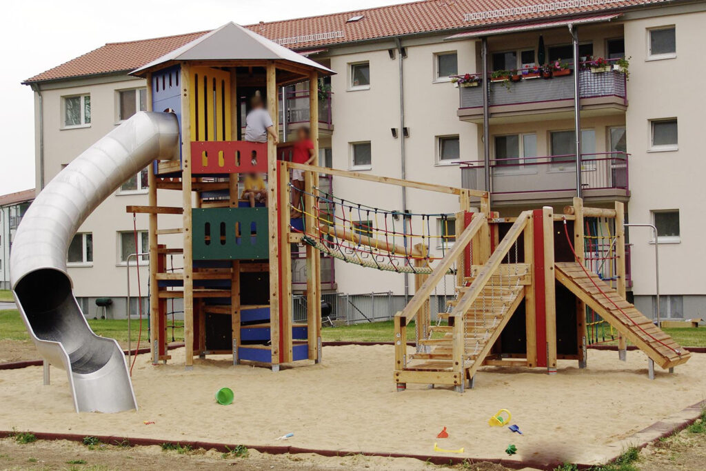 Moderner Kinderspielplatz mit Kletterturm und Rutsche vor Wohngebäude, errichtet durch Gerhäuser Bau, spezialisierte Baufirma für Massivbau in Mittelfranken.